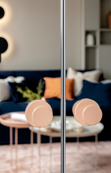 The mirrored front of a cabinet with round, orange handles.